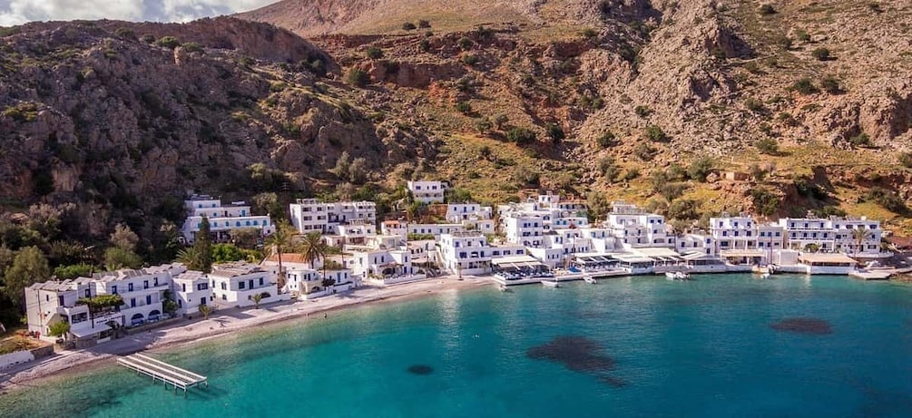 A coastal village with white buildings, a pier, and clear turquoise waters. 2