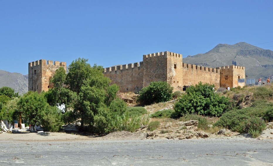 A historic stone castle with multiple towers, surrounded by greenery and mountains in the background. 5
