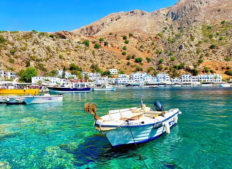 A coastal village with boats docked in clear blue waters, surrounded by rocky hills and white buildings. 1