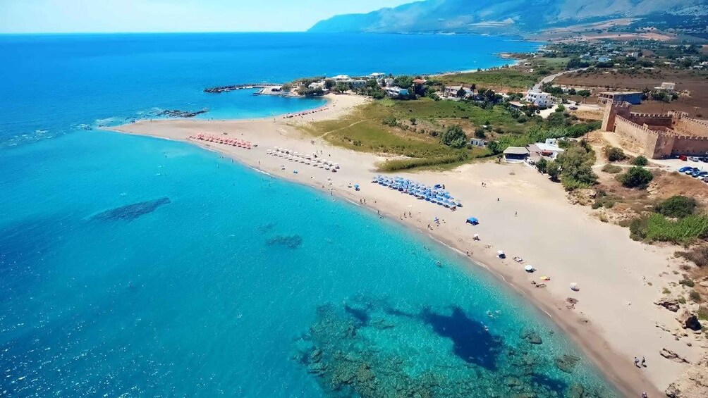 A coastal beach with clear turquoise waters, a sandy shore, and a castle-like structure on the right. 3