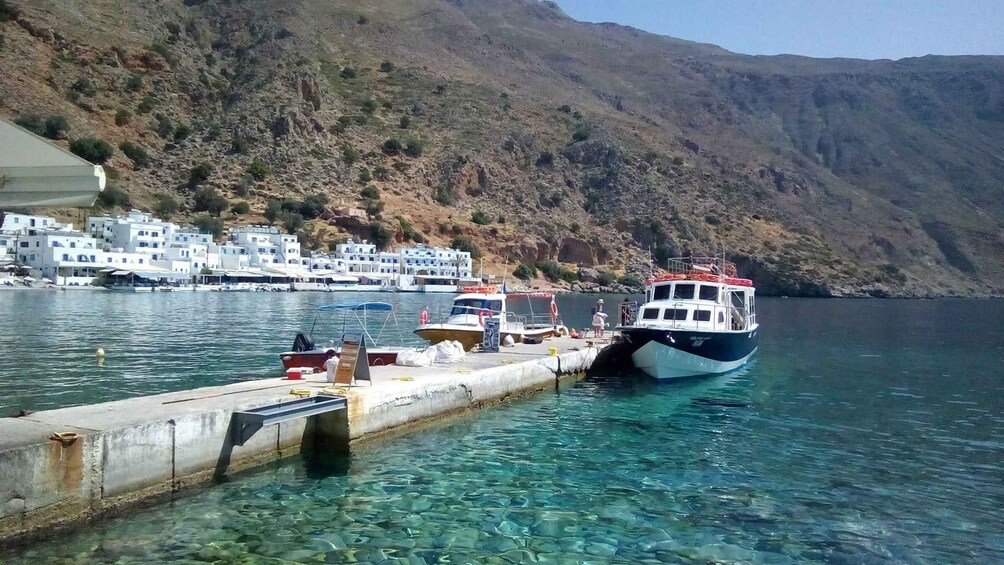 A boat docked at a pier with clear water, a mountainous backdrop, and white buildings along the shore. 5