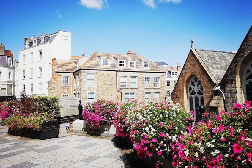 A town square with historic buildings, a church, and blooming flowers. 2