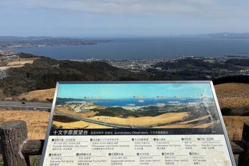 Un belvédère offrant une vue panoramique sur la côte, un panneau d’information avec du texte, et un ciel dégagé. 3