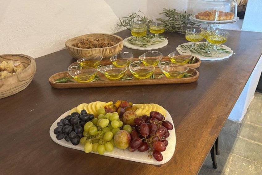 Ett träbord med en fat med frukt, glas med olivolja och bröd. 4