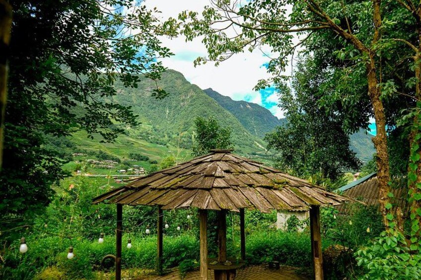 A wooden gazebo in a lush green landscape with mountains in the background. 4