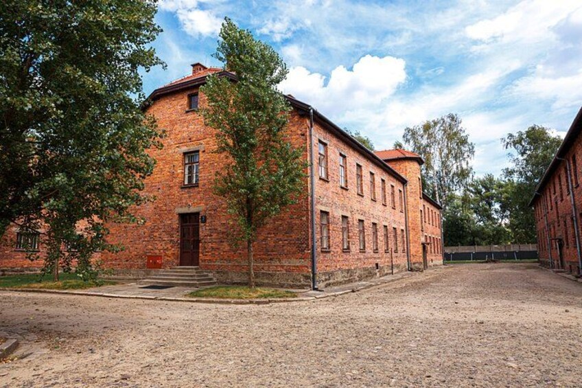 Een gebouw van baksteen met een rood dak, omringd door bomen en een grindpad. 5