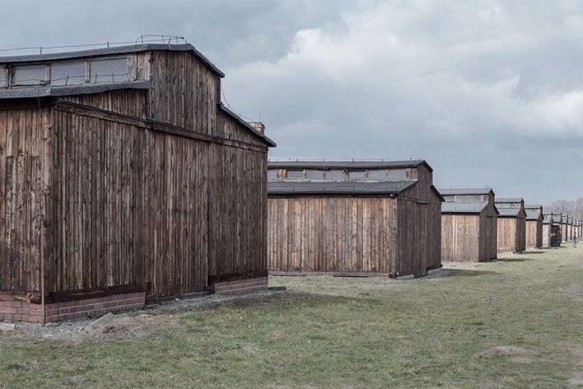 Een rij houten gebouwen met een grasveld op de voorgrond. 3