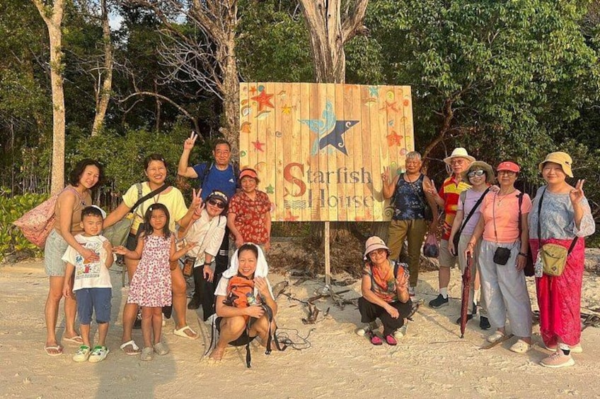 A group of people posing in front of a wooden sign with a starfish and a fish design, indicating a Starfish House. 2