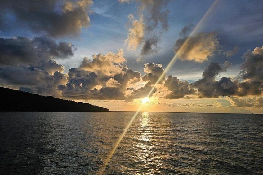 A sunset over a body of water with clouds and a silhouette of a landmass. 5