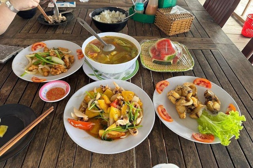 A wooden table with various dishes including a bowl of soup, plates of stir-fried vegetables, and grilled fish. 4