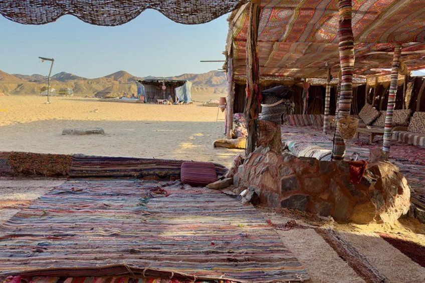 A traditional tent with colorful rugs and cushions, set against a desert landscape with mountains in the background. 2