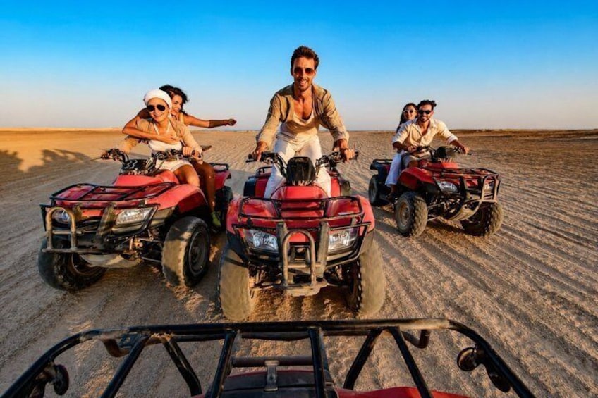 Three people on red ATVs in a desert with clear skies. 2