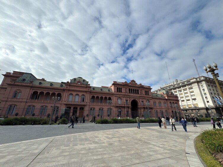 A historic building with arched windows and a central archway, surrounded by a paved plaza with people walking. 5