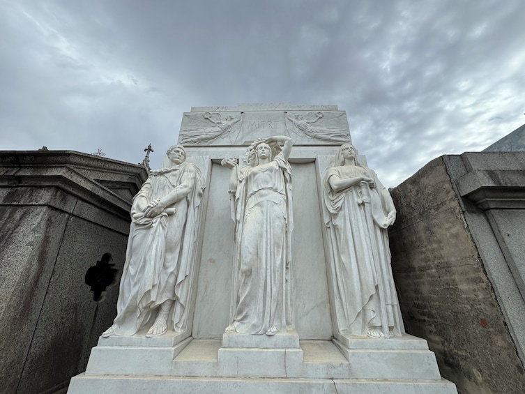 A marble monument with three figures, one central and two flanking, under a cloudy sky. 3