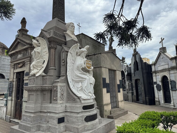 A cemetery with a prominent monument featuring angel statues and a plaque reading 'FATHER FAITHY.' 2