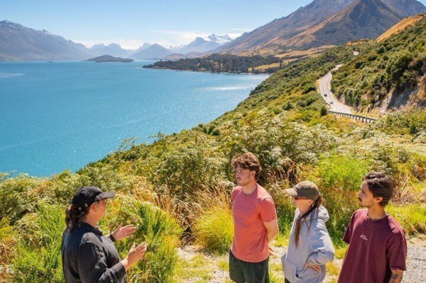 Eine Gruppe von Menschen steht auf einem Hügel und blickt auf einen See mit Bergen im Hintergrund. 3