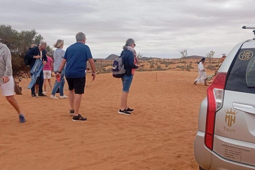 A group of people walking on a sandy terrain with a car parked nearby. 1