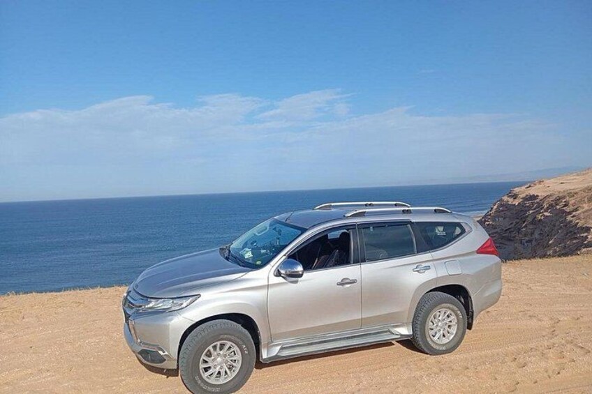 A silver SUV parked on a sandy beach with the ocean in the background. 4