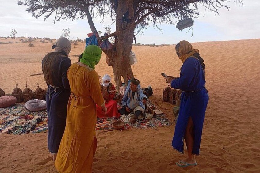 A group of people gathered around a tree in a desert setting. 2