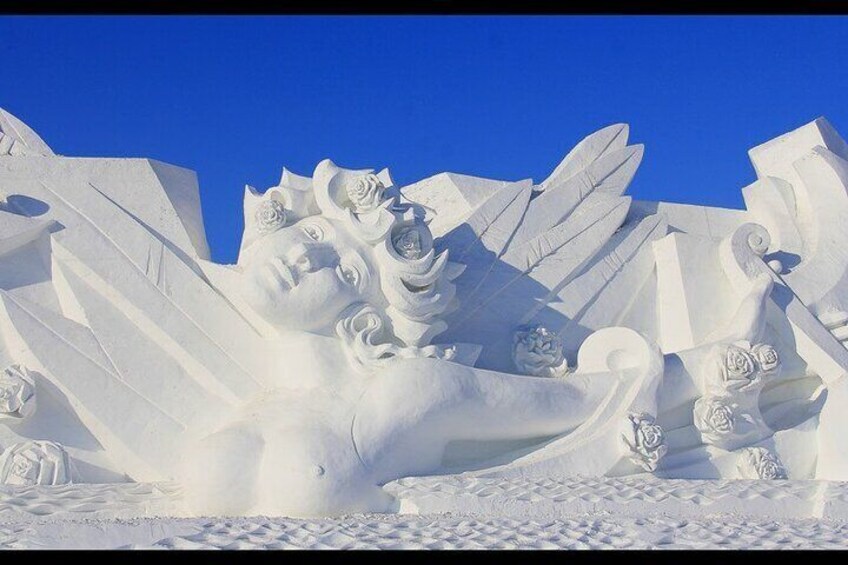 A large snow sculpture of a reclining figure with wings and roses. 4