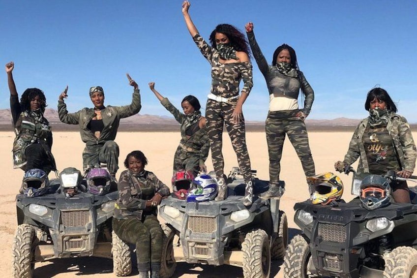 A group of people in military-style camouflage attire posing on ATVs in a desert landscape. 1
