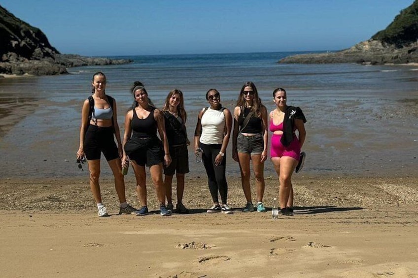A group of people standing on a sandy beach with a rocky shoreline and calm water in the background. 4