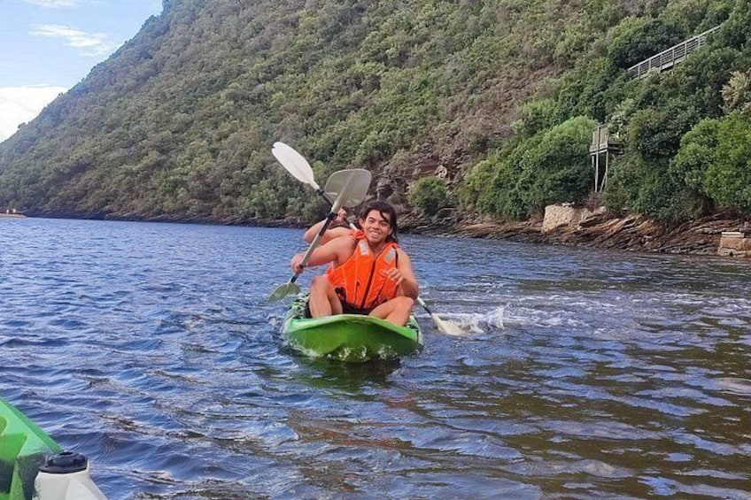 A person kayaking on a river with a forested hillside in the background. 2
