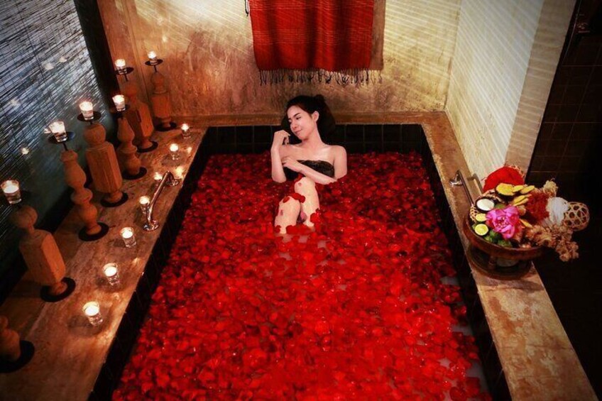 Una mujer en una bañera llena de pétalos de rosa roja, rodeada de velas y candelabros de madera. 1