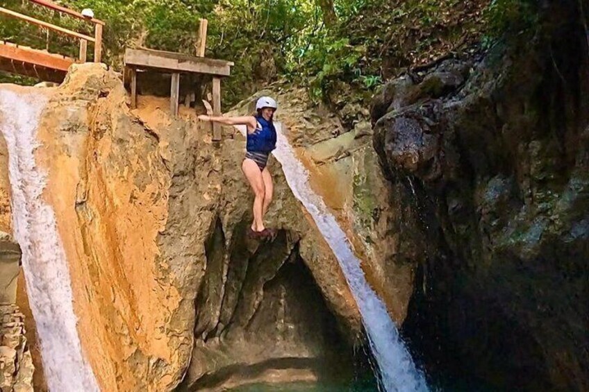 Eine Person steht auf einem Felsvorsprung, oberhalb befindet sich eine Holzplattform, mit Blick auf einen Wasserfall. 3
