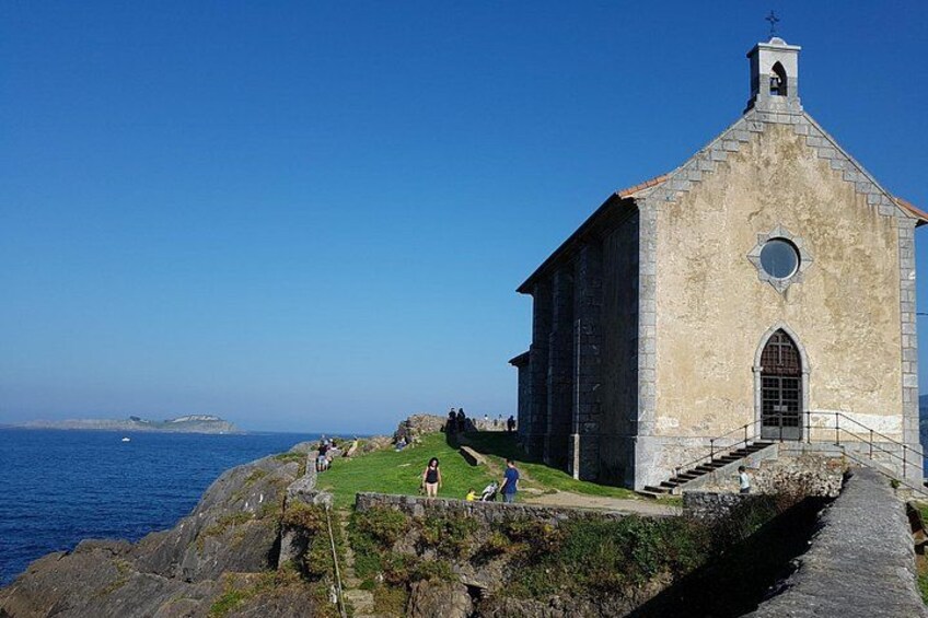 Une église côtière avec une façade en pierre, un petit clocher et un espace verdoyant où se trouvent des personnes. 3