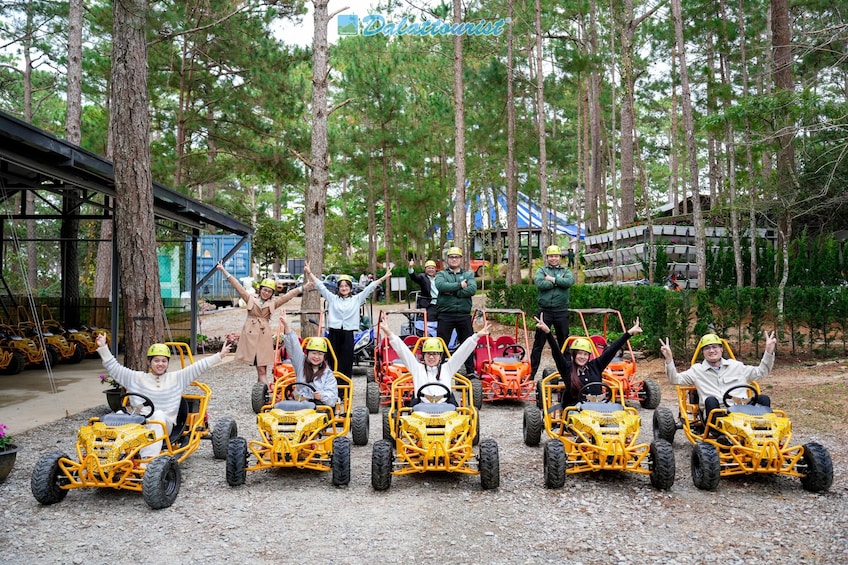Ihmiset istuvat keltaisissa, moottoroiduissa lastenautoissa, ja heillä on kädet koholla. Heidän ympärillään on puita ja sinikattoinen rakennus. 4