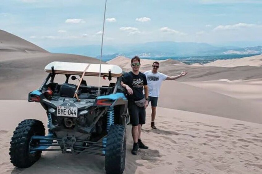 Ein Geländewagen auf einer Sanddüne, neben dem zwei Personen stehen. 4
