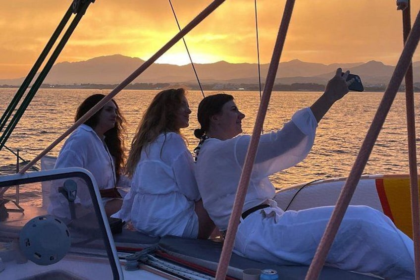 Three people on a sailboat during sunset with mountains in the background. 1