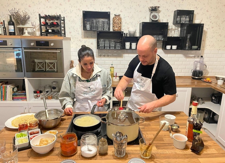 Two people cooking in a kitchen with various ingredients and utensils on the counter. 1