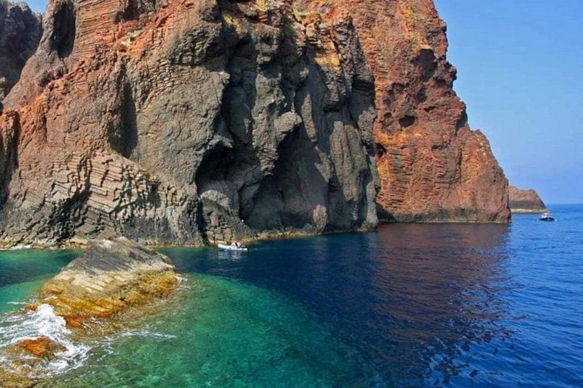 A rocky coastline with clear blue water, a small boat, and a distant ship. 5