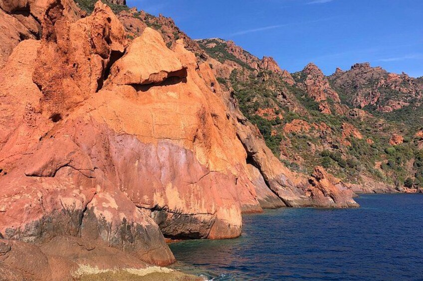 A coastal landscape with reddish-brown cliffs and a calm sea. 3