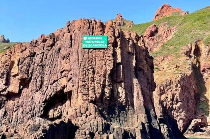 Una scogliera rocciosa con un cartello che riporta la scritta 'RESERVA NATURALE DE SCANDOL'. 3