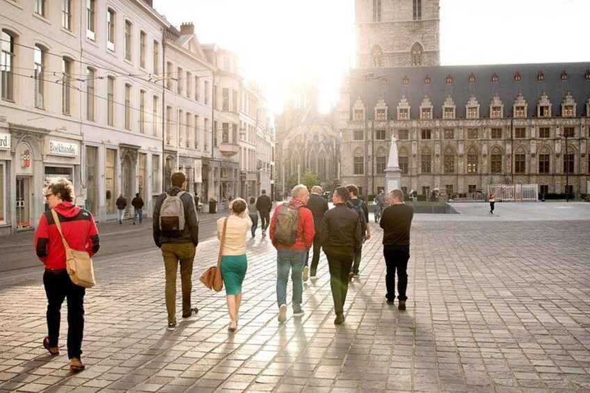 Een groep mensen loopt over een geplaveid plein, met historische gebouwen op de achtergrond. 3