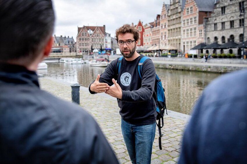 Een man met een rugzak staat bij een gracht, met gebouwen op de achtergrond. 2