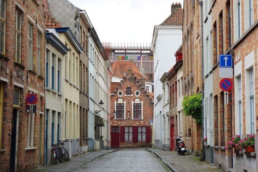 En kullerstensgata med historiska byggnader, en röd dörr och en blå vägvisningsskylt. 3