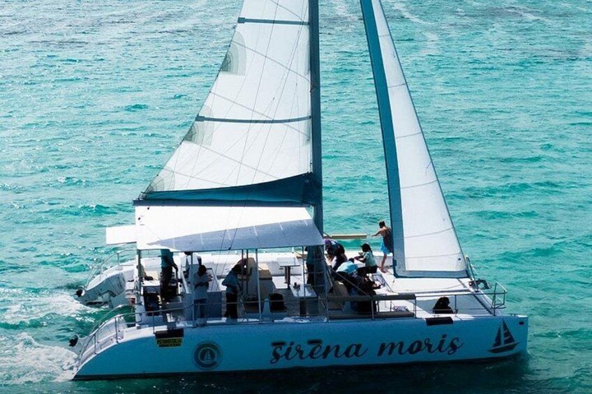 A sailboat named 'Sirena moris' with a white hull and blue sails, sailing on turquoise waters. 2