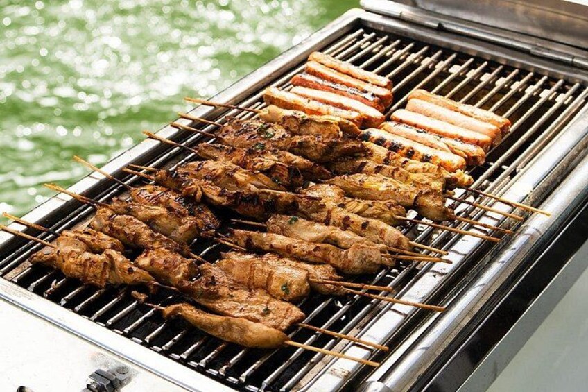 Skewers of meat grilling on a barbecue over water. 3