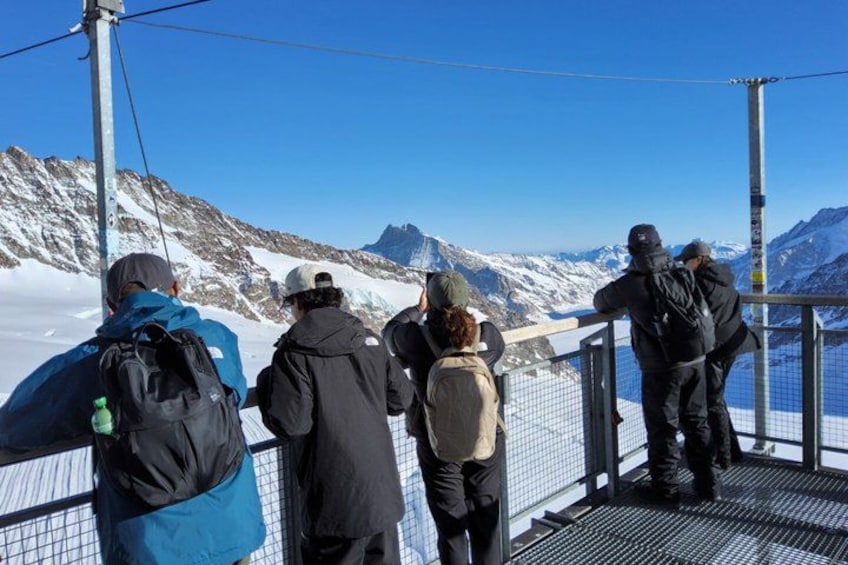 Un grupo de personas en una plataforma metálica con vistas a un paisaje montañoso nevado. 2