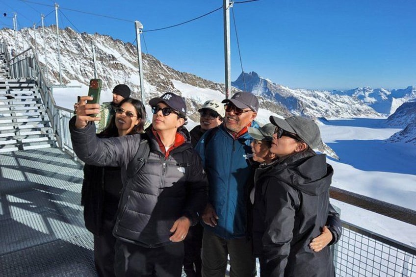 Un groupe de personnes prenant un selfie sur un sentier de montagne enneigé, avec un glacier en arrière-plan. 3