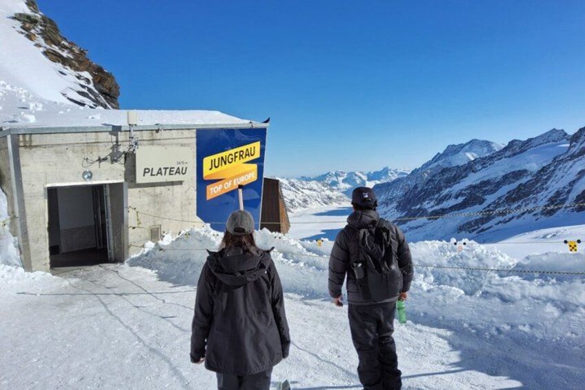Dos personas caminando hacia un cartel que dice 'Jungfrau Top of Europe' en una montaña nevada. 3