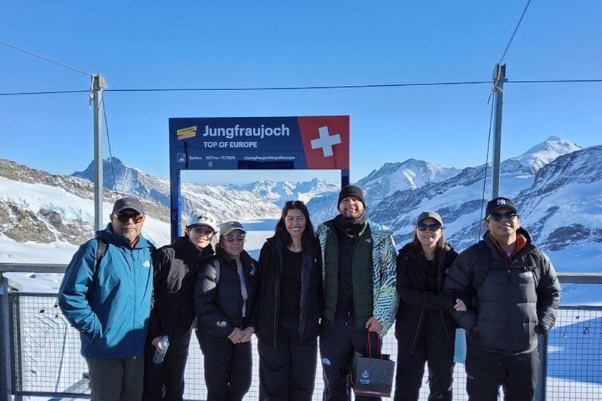 Un gruppo di persone in piedi di fronte a un cartello con su scritto 'Jungfraujoch Top of Europe' e una bandiera svizzera. 1