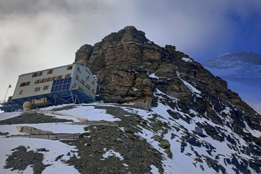 Una montagna con un edificio su un pendio, chiazze di neve e terreno roccioso. 2