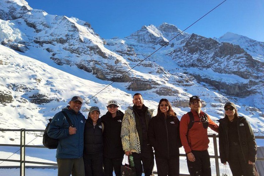Un groupe de personnes se tient sur une montagne enneigée, sous un ciel dégagé, avec des montagnes rocheuses en arrière-plan. 2