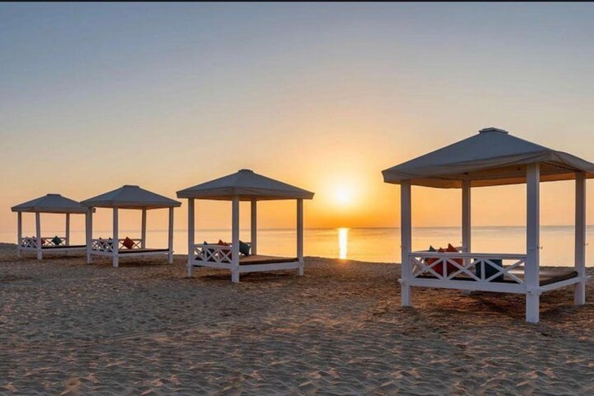 A beach with four white gazebos and a sunset in the background. 2