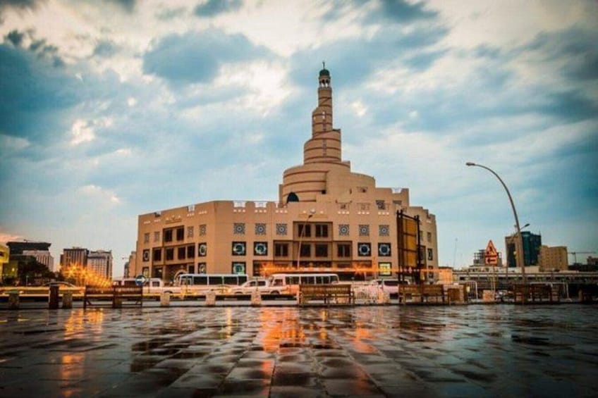A large building with a prominent tower, surrounded by a wet reflective surface, possibly a plaza or street. 1